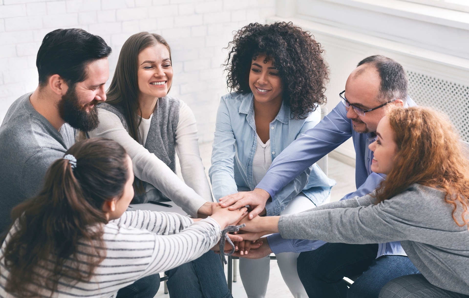 Happy rehab group patients connecting hands at therapy session